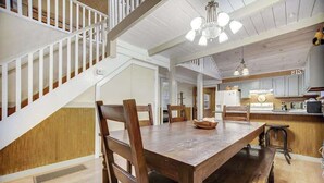 Una mesa de comedor de madera con sillas, una escalera y una zona de cocina con armarios y electrodomésticos.