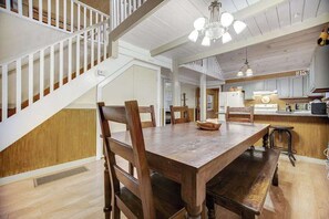 Una mesa de comedor de madera con sillas, una escalera y una zona de cocina con armarios y electrodomésticos.