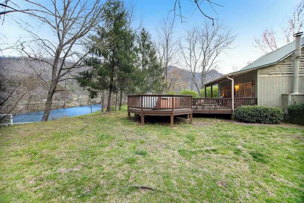 A house with a deck overlooking a body of water, surrounded by trees and a hilly landscape.