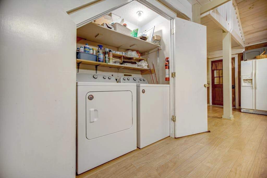 A compact laundry room with a washing machine, dryer, and shelves above containing cleaning supplies.