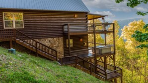 A log cabin with a stone foundation, a wooden deck, and a metal railing. - Sun Eagle Lodge (Bryson City)
