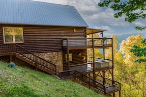 Eine Blockhütte mit Steinunterbau, einer Holzterrasse und einem Metallgeländer.