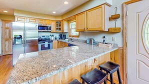 A kitchen with granite countertops, stainless steel appliances, wooden cabinets, and a bar stool area. - Sun Eagle Lodge (Bryson City)