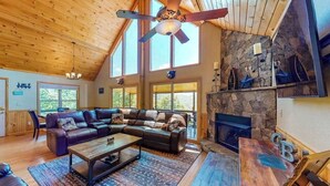 A spacious living room with a stone fireplace, leather sofa, and a ceiling fan. - Sun Eagle Lodge (Bryson City)