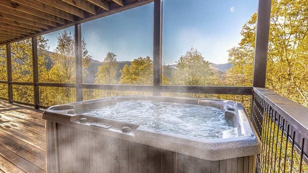 A hot tub on a wooden deck with large windows overlooking a forested area. - Sun Eagle Lodge (Bryson City)