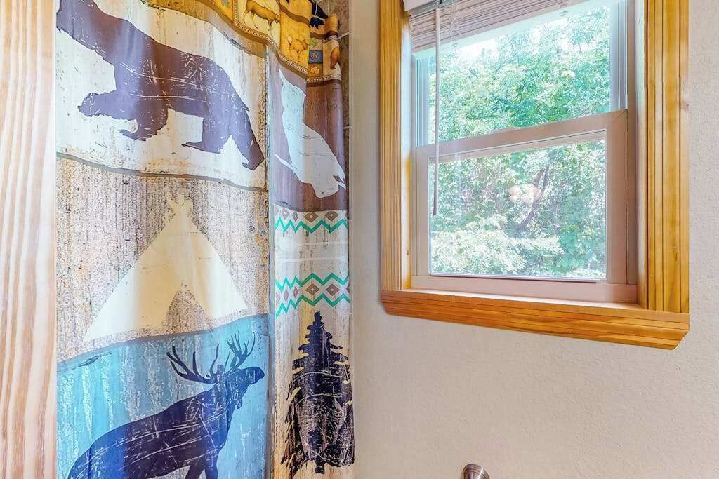 Una habitación con un amplio ventanal, cortina con estampados de fauna y vistas al verdor exterior.