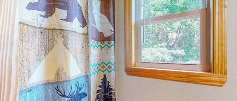 Una habitación con un amplio ventanal, cortina con estampados de fauna y vistas al verdor exterior.