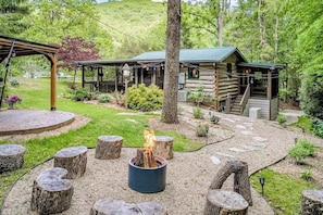 Eine rustikale Holzhütte mit Feuerstelle, einer Holzterrasse und einer überdachten Sitzgruppe im Freien.