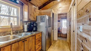 A wooden cabin interior with a kitchen area, including a refrigerator, coffee maker, and wooden cabinets.