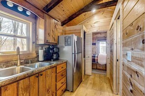 Innenansicht einer Holzhütte mit einer Küchenzeile, darunter ein Kühlschrank, eine Kaffeemaschine und Holzschränke.