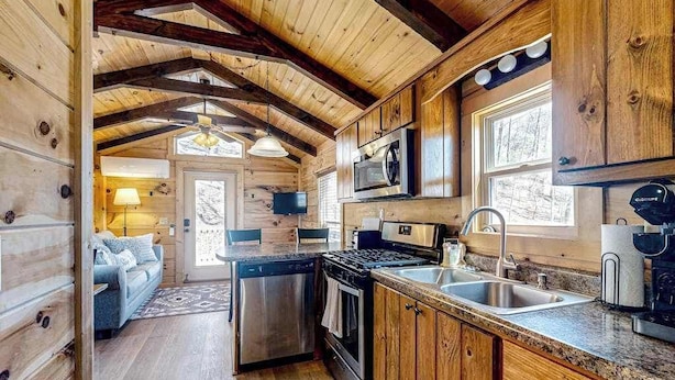 A cabin interior with a kitchen, dining area, and a living room with a fireplace.