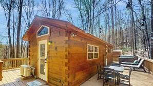 A wooden cabin with a deck, a table, chairs, and a hot tub.