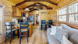 A log cabin interior with a kitchen, dining area, and a sofa with pillows.