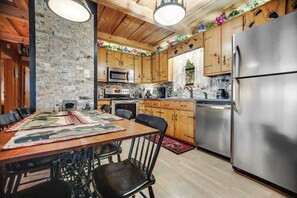 A kitchen with wooden cabinets, a stainless steel refrigerator, and a dining table with chairs. - Black Bear cabin fox Mountain (Franklin)