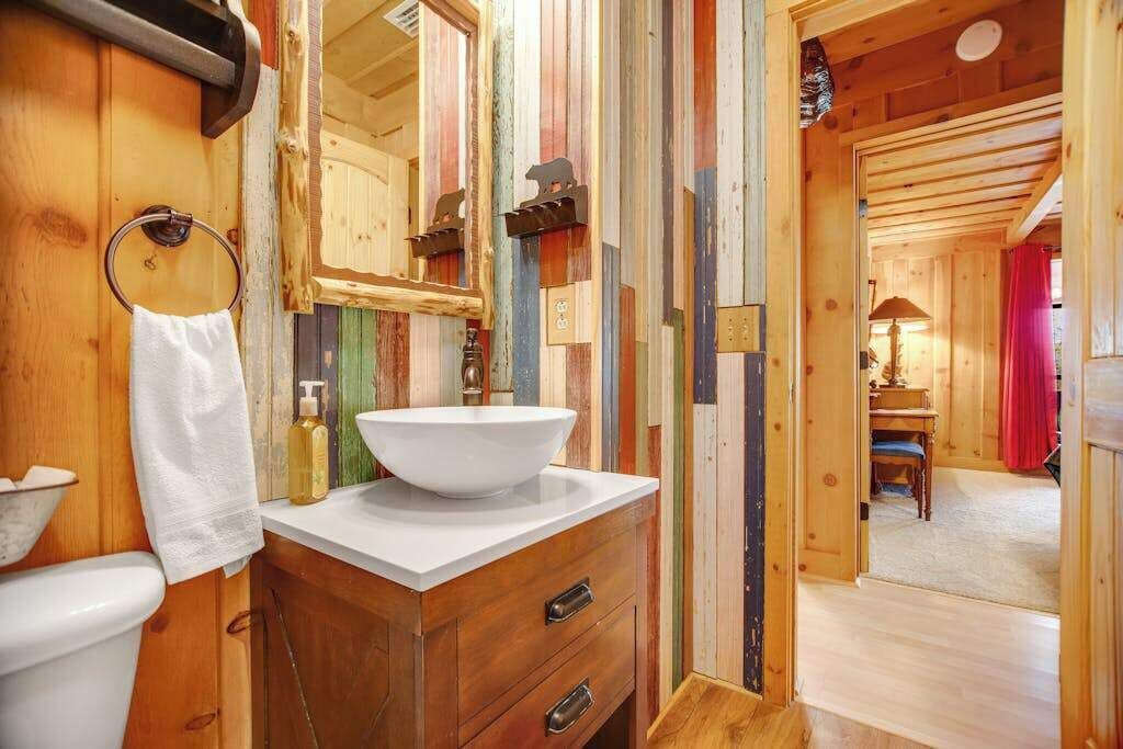 Un interior de madera con un lavamanos blanco, armarios de madera, un espejo y un perchero para toallas.