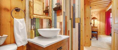 Un interior de madera con un lavamanos blanco, armarios de madera, un espejo y un perchero para toallas.