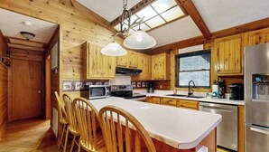 Eine holzhausartige Küche mit Kochinsel, Holzkästen, einem Edelstahlkühlschrank und einem Fenster mit Jalousien.