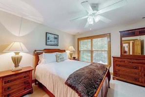 Ein Schlafzimmer mit Bett, Nachttischen, einer Kommode, einem Deckenventilator, einem Fenster mit Jalousien und einem gerahmten Bild an der Wand.