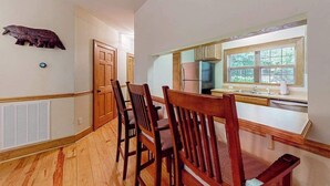 Un comedor con sillas de madera, una cocina con ventana y una decoración con un oso en la pared.