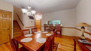 Comedor con mesa de madera, sillas, una lámpara de araña y una escalera.