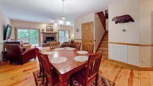 Un comedor con una mesa y sillas de madera, una chimenea y una escalera que sube a otro nivel.