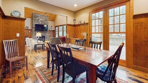 A dining area with a wooden table and chairs, a stone fireplace, and a television. - Tuckaway Retreat (Sylva)