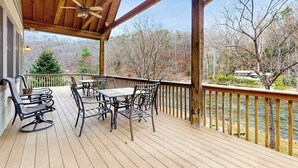 A wooden deck with outdoor furniture, a ceiling fan, and a view of a river and trees. - Tuckaway Retreat (Sylva)