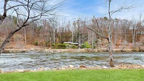 A river with a grassy bank and trees in the background. - Tuckaway Retreat (Sylva)