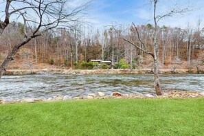 Ein Fluss mit einer grasbewachsenen Uferböschung und Bäumen im Hintergrund.