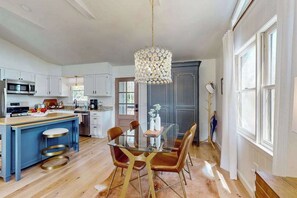 A modern kitchen with a central island, a dining area with a glass table, and a large window providing natural light. - Cashmere Cottage (Cashiers)