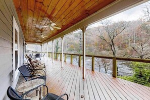 Eine Holzterrasse mit Stühlen und einem Tisch, mit Blick auf einen Fluss und Bäume.