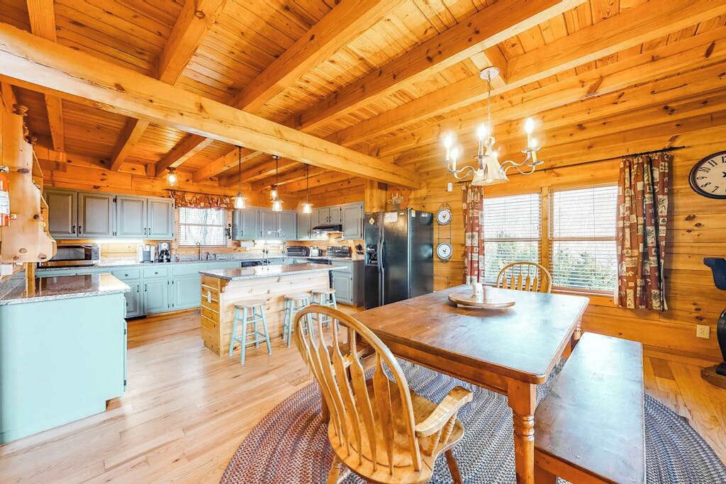 A wooden cabin interior with a kitchen, dining area, and a large window.