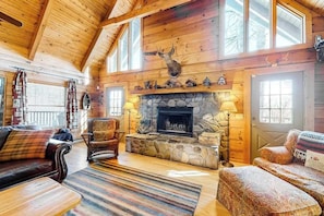 A log cabin interior with a stone fireplace, wooden ceiling beams, and a deer head mounted above it. - Secluded cabin with mountain views, fire pit & billiards (Sylva)