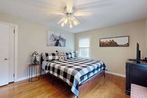 Ein Schlafzimmer mit Bett, Deckenventilator, Fenster und Bildern an der Wand.