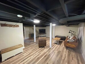Ein Zimmer mit Holzboden, einem braunen Sofa, einem kleinen Tisch, einem Fernseher und einer weißen Säule.