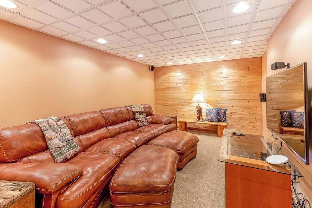 Una habitación con un sofá de cuero marrón, una mesa de centro de vidrio, una pared de madera y un televisor de pantalla plana montado en la pared.