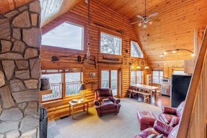 Ein Blockhaus-Interieur mit Kamin aus Stein, Holzwänden, einem Essbereich und einer Sitzecke mit Ledersofas.