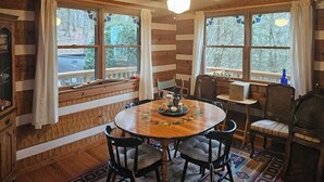A wooden cabin interior with a dining table, chairs, and a ceiling fan. - Rocky Knob Getaway (Scaly Mountain)