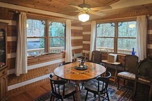 A wooden cabin interior with a dining table, chairs, and a ceiling fan. - Rocky Knob Getaway (Scaly Mountain)