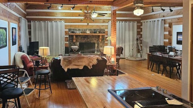 A cozy living room with a fireplace, wooden floors, a dining area, and a kitchen with a stove. - Rocky Knob Getaway (Scaly Mountain)