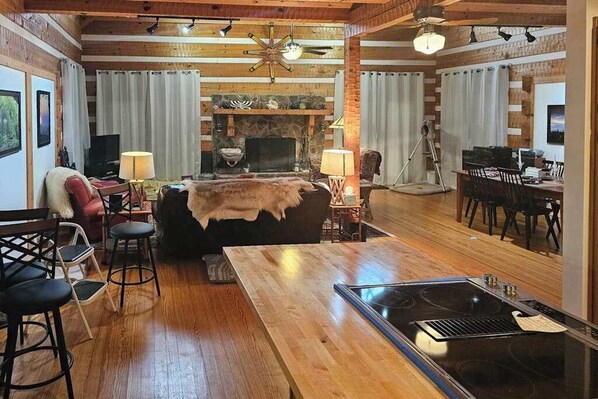 A cozy living room with a fireplace, wooden floors, a dining area, and a kitchen with a stove. - Rocky Knob Getaway (Scaly Mountain)
