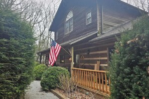 A wooden cabin with a porch, an American flag, and dense greenery. - Rocky Knob Getaway (Scaly Mountain)