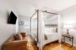 A four-poster bed with a canopy, a television mounted on the wall, a bedside table with a lamp, and a leather sofa. - Stephen Cottage (Highlands)