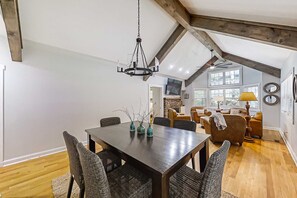 A dining area with a wooden table and chairs, a hanging light fixture, and a view of the living room with a sofa and chairs. - Stephen Cottage (Highlands)
