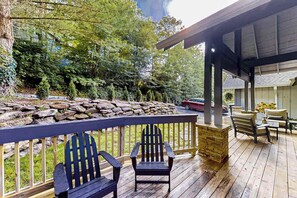 A wooden deck with Adirondack chairs, a stone wall, and a covered area with a sofa and table. - Stephen Cottage (Highlands)