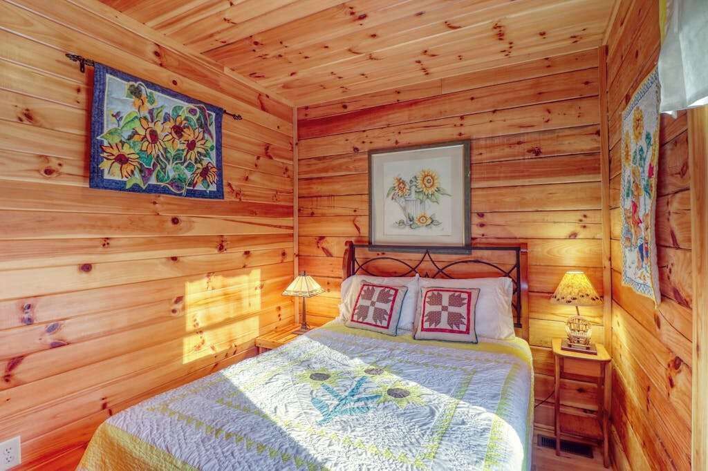 Een slaapkamer in een houten chalet, met een bed, twee bedlampen en bloemenkunst aan de muur.
