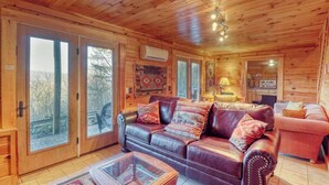 Interno di una baita di legno con un divano in pelle, un tavolino da caffè in vetro e un'area pranzo.