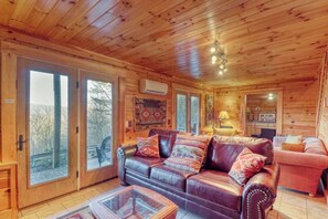 A wooden cabin interior with a leather sofa, a glass coffee table, and a dining area. - Bear Bottoms Welcome (Whittier)