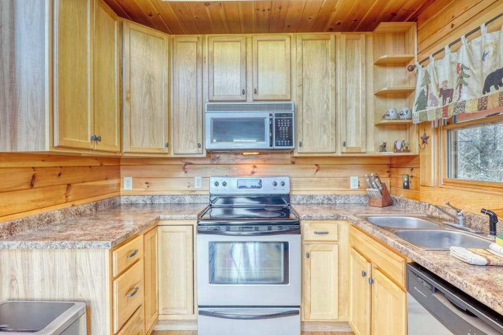 Una cucina con mobili in legno, un forno a microonde, un forno, piani di lavoro in granito e una finestra con vista.