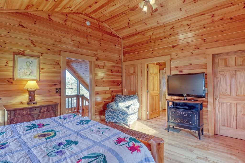 A wooden cabin room with a bed, a television, a chair, and a dresser.